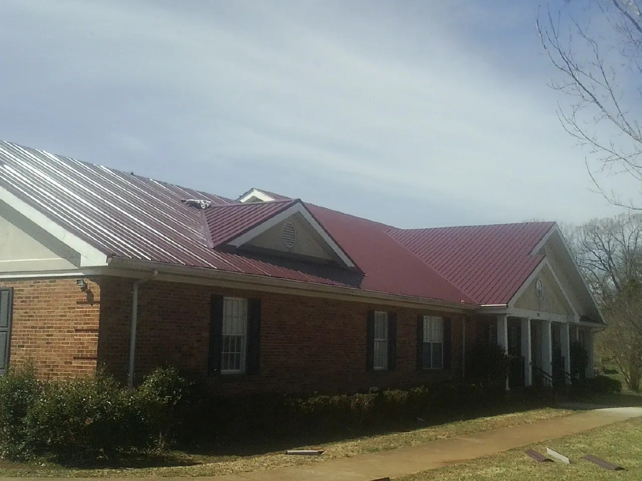 Red metal roof with gabled entries on a long brick building, from a Hail Damage Roof Repair job in Union